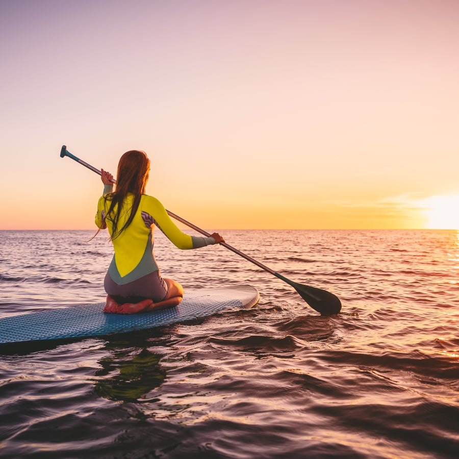 Girl on stand up paddle board, quiet sea with warm sunset colors.
