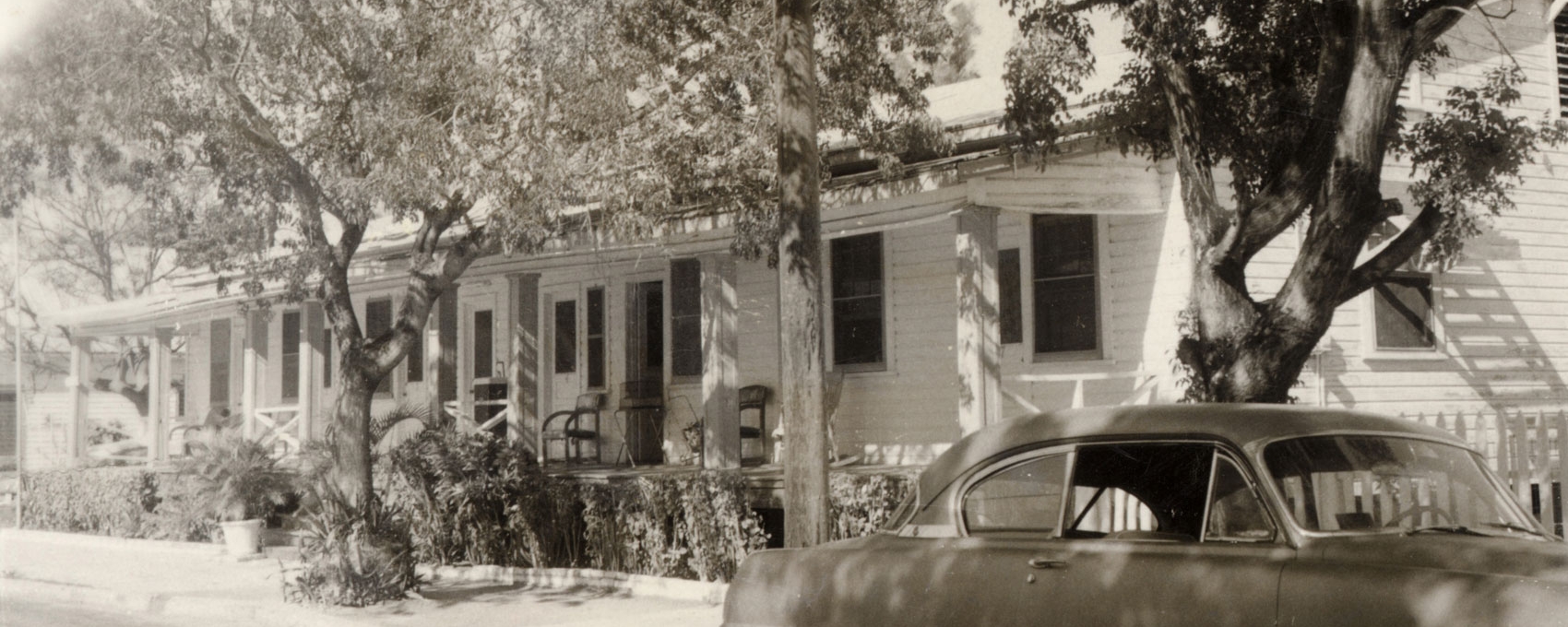 A historic photo of the Merlin Hotel with an antique car parked out front.