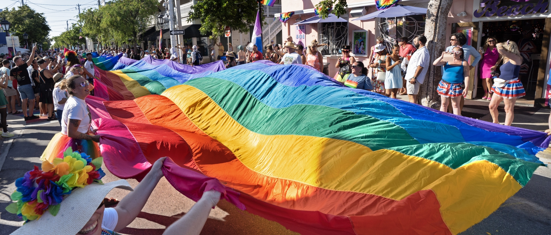 A large rainbow flag being held up individuals during a pride parade on Duval Street.