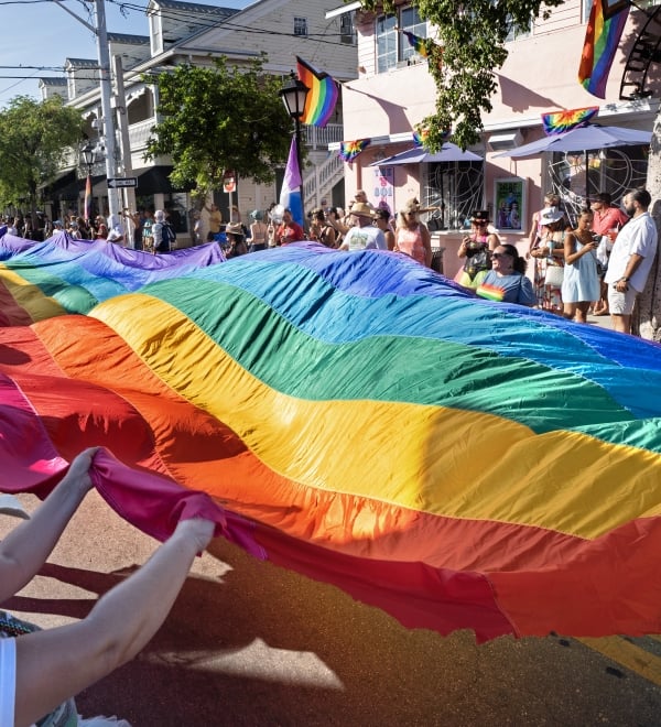 A large rainbow flag being held up individuals during a pride parade on Duval Street.